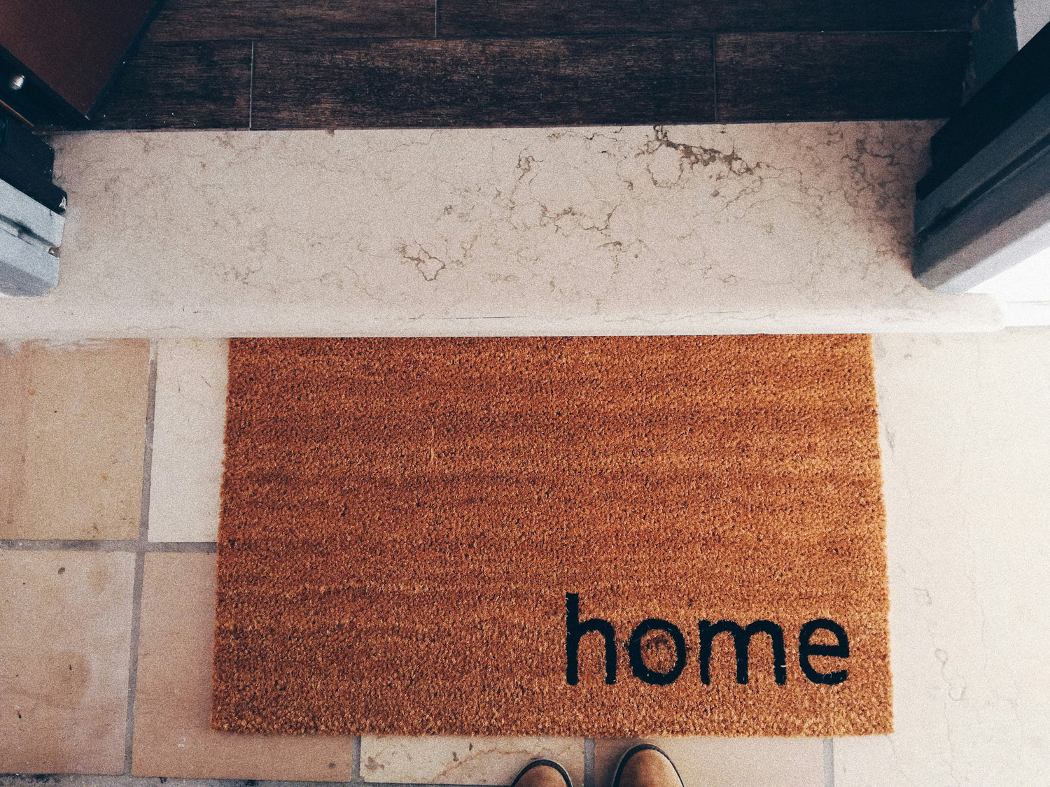 Top view of a brown welcome doormat with the word ‘home’ placed at a clean entryway